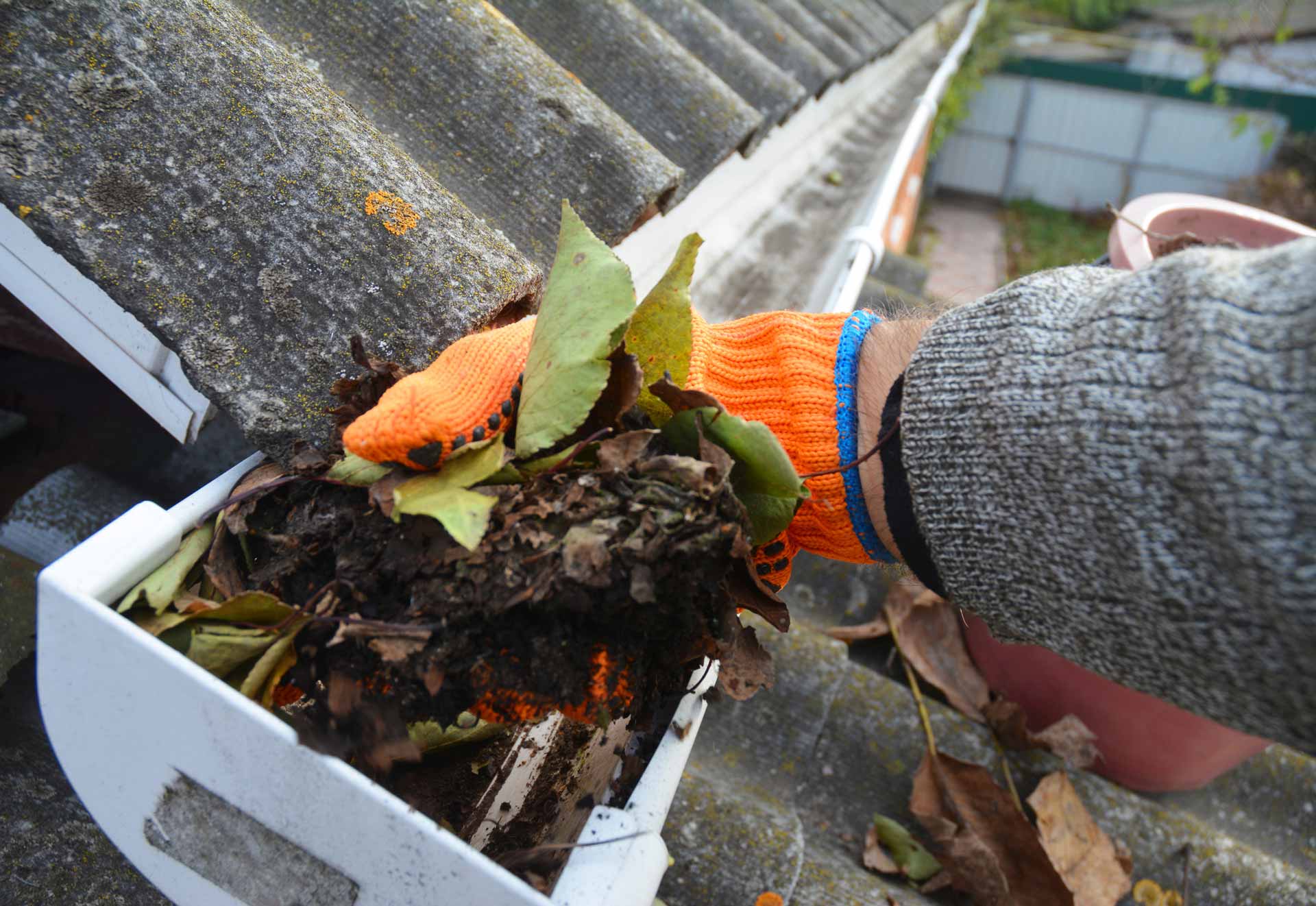 Gloved hand cleaning dirt and leaves out of rain gutters