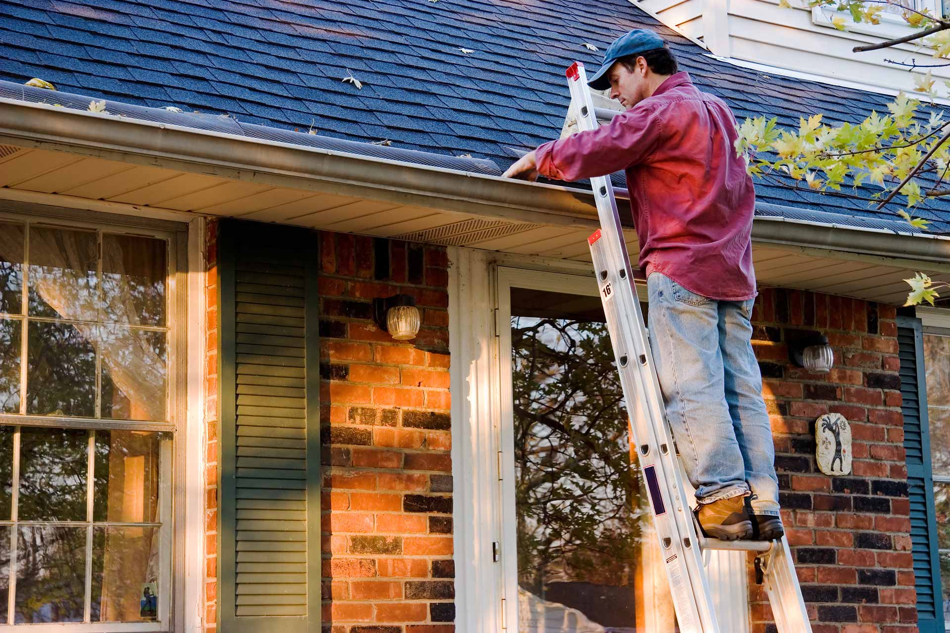Man on ladder inspecting rain gutters